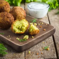 Chrupiące kulki falafel kebab na desce, obok sosu i świeżego koperku.