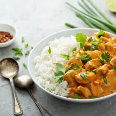 Kurczak w sosie curry z ryżem, posypany szczypiorkiem i kolendrą. Obok miseczka z chili i limonka.