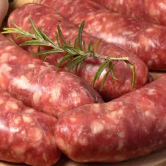 Świeża salsiccia z gałązką rozmarynu i czosnkiem w tle, gotowa do grillowania.