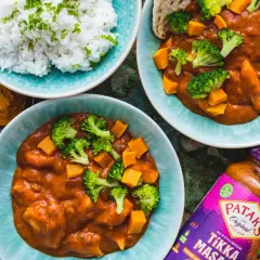 Dwa talerze z indyjskim curry z dynią i brokułami, ryżem i słoikiem sosu Tikka Masala.