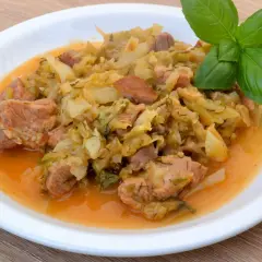 Pyszny bigos z młodej kapusty z mięsem i kiełbasą, podany na białym talerzu, ozdobiony gałązką bazylii. Idealny przepis, jak ugotować dobry bigos z młodej kapusty.