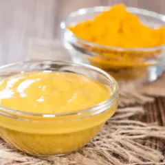 Gotowe składniki do pasty curry: gładka, żółta pasta w miseczce i sypka kurkuma w tle.