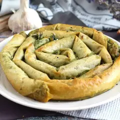 Złocisty borek ze szpinakiem, zwinięty w spiralę, prezentuje się apetycznie na białym talerzu. W tle czosnek i cebulka.
