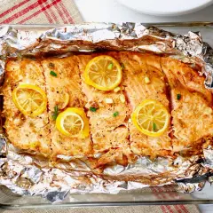 Pyszny, pieczony filet z łososia z plasterkami cytryny i szczypiorkiem, podany w folii aluminiowej.
