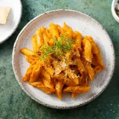 Penne z kremowym, aromatycznym **czerwonym pesto**, posypane parmezanem i udekorowane świeżymi ziołami.