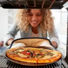 Uśmiechnięta kobieta wyjmuje z piekarnika pyszną pizzę. Idealna temperatura pieczenia pizzy to klucz do sukcesu!