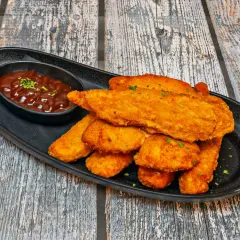 Chrupiący sznycel z kurczaka w panierce, podany z sosem barbecue na czarnej tacy.