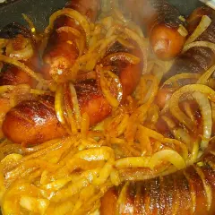 Gorąca, rumiana kiełbasa z cebulą dusi się na patelni, tworząc apetyczny aromat.