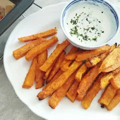 Frytki z batatów na białym talerzu z dipem, obok blacha z frytkami.
