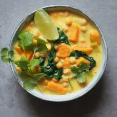 Aksamitne curry z ciecierzycy z kawałkami batata i szpinaku, ozdobione świeżą kolendrą i ćwiartką limonki.