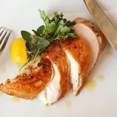 Soczysty kurczak sous vide, pokrojony w plastry, z cytryną i ziołami na białym talerzu. Obok widelec i nóż.