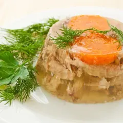 Tradycyjna galareta wieprzowa z marchewką i koperkiem, podana na białym talerzu.