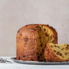 Puszysta babka włoska z rodzynkami, pokrojona na talerzu, obok widelec.