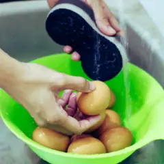 Ręce myją jajka w zielonej misce pod bieżącą wodą, przygotowując je do tego, jak sparzyć jajka.