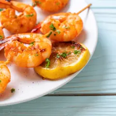 Pyszne krewetki z airfryer, podane na talerzu z plasterkiem cytryny i posypane natką pietruszki.