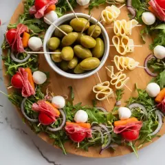 Oto 10 najlepszych sałatek na imprezę: przekąski z mozzarellą, salami, pomidorkami i oliwkami na desce z rukolą.