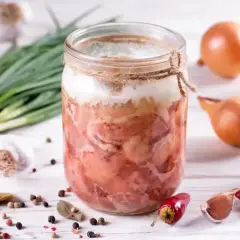 Słoik z domową kiełbasą w galarecie, obok cebula, czosnek, pieprz i chili. Idealny przepis na to, jak zrobić kiełbasę w słoiku z galaretką.
