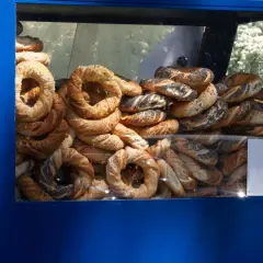 Stos świeżych obwarzanków w niebieskiej budce. Widać obwarzanki z makiem, sezamem i posypką serową.