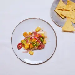Kolorowe ceviche z owocami cytrusowymi, ananasem, papryczką chili i czerwoną cebulą, podane na talerzu obok nachos.