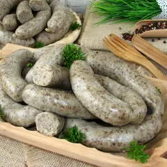 Pyszna, domowa biała kaszanka ułożona na drewnianej desce, ozdobiona natką pietruszki. Obok widoczne drewniane sztućce i przyprawy.