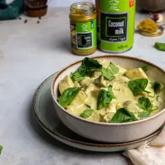 Miseczka zielonego curry z kurczakiem i szpinakiem, obok puszka mleka kokosowego i słoiczek pasty curry.
