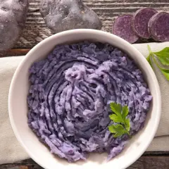 Fioletowe ziemniaki w misce, obok kilka sztuk i plasterki. Pyszne purée z fioletowych ziemniaków.