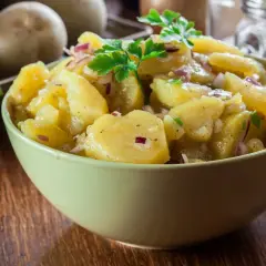 Pyszna sałatka bawarska z ziemniaków, cebuli i natki pietruszki, podana w zielonej misce na drewnianym stole.