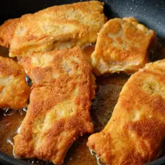 Pięć kawałków panierowanej ryby smaży się na złoty kolor na patelni. Idealny sposób, jak smażyć rybę, by była chrupiąca.