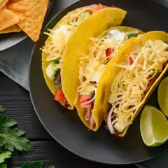 Pyszne tacos z kurczakiem, z serem, warzywami i limonką. Obok nachos i natka pietruszki.