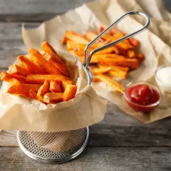 Chrupiące frytki z batatów w koszyku, z ketchupem i majonezem na papierze.