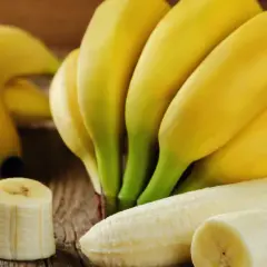 Pęczek żółtych bananów i kilka plasterków na drewnianym blacie. Banany właściwości odżywcze czynią je idealną przekąską.