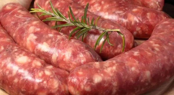 Świeża salsiccia z gałązką rozmarynu i czosnkiem w tle, gotowa do grillowania.