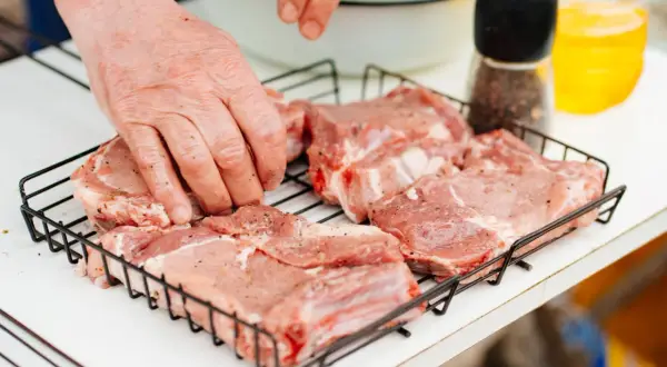 Ręce doprawiające mięso na ruszcie. Zastanawiasz się, ile peklosoli na kilogram mięsa?