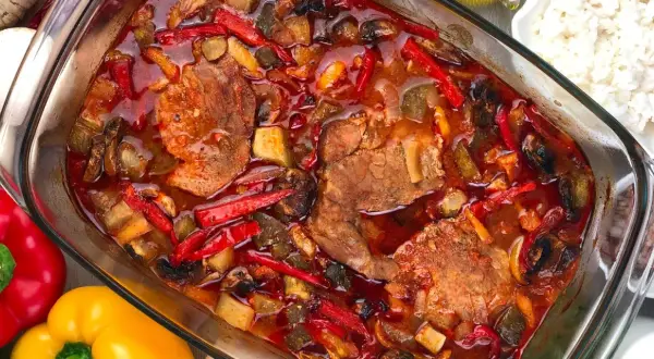 Karkówka po zbójnicku w plastrach, duszona z papryką, pieczarkami i cebulą w aromatycznym sosie. Obok miseczka ryżu.