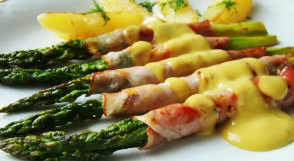 Zielone szparagi owinięte w szynkę parmeńską, polane sosem holenderskim, z ziemniakami.