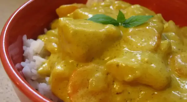 Miseczka czerwona z ryżem i kremowym, żółtym curry z kawałkami kurczaka i marchewki, ozdobiona listkiem mięty.