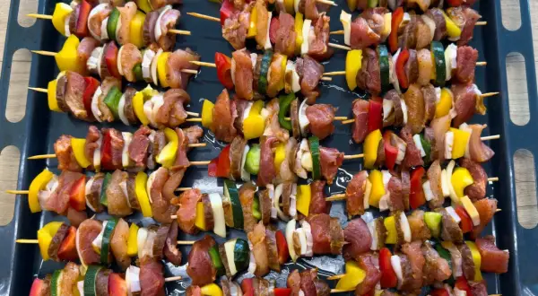 Szaszłyki w piekarniku: mięso, papryka, cebula i cukinia na patyczkach, gotowe do pieczenia.