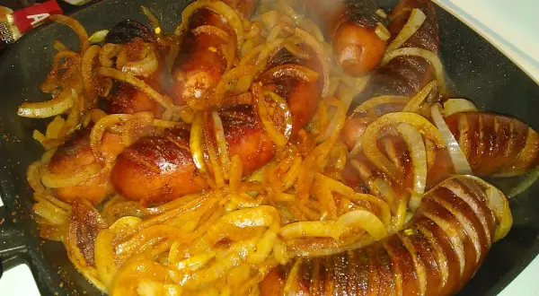 Gorąca, rumiana kiełbasa z cebulą dusi się na patelni, tworząc apetyczny aromat.