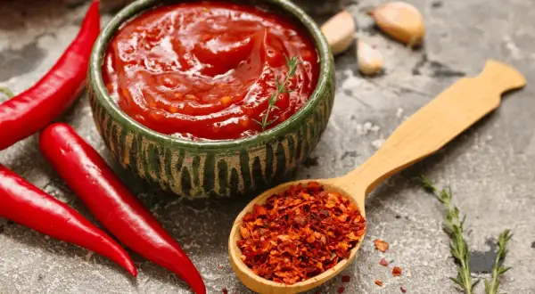 Miseczka pełna pikantnego sosu meksykańskiego, obok świeże papryczki chili i drewniana łyżka z płatkami chili.
