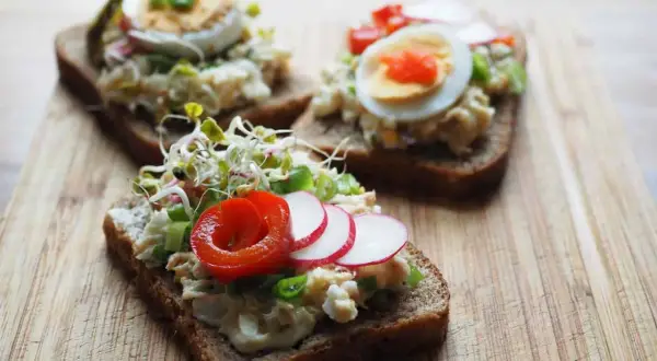 Pyszna pasta jajeczna z makrelą na ciemnym pieczywie, udekorowana kiełkami, rzodkiewką i papryką. Idealna na szybkie śniadanie.