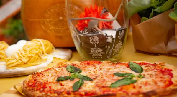 Pyszne rodzaje pizzy, makaron i ser parmezan. W tle szklany wazon z dekoracjami i kwiatami.