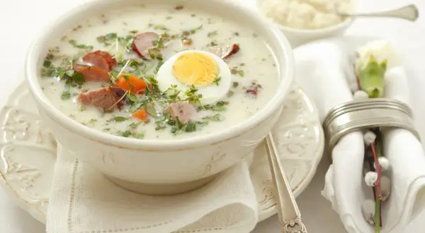 Aromaticzny żurek z białą kiełbasą i jajkiem, podany w białej misce. Idealny prosty przepis na wielkanocne śniadanie.
