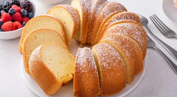 Puszysta babka wielkanocna, posypana cukrem pudrem, z miseczką owoców leśnych obok. Idealna na święta, gdy szukasz prostego przepisu.