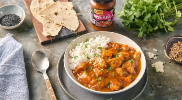 Pyszny kurczak tikka masala z ryżem, podany z plackami i świeżą kolendrą. Idealny na szybki obiad.