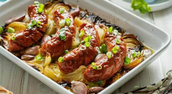 Pyszna, pieczona biała kiełbasa z cebulą i czosnkiem, posypana szczypiorkiem. Idealna na wielkanocny stół.