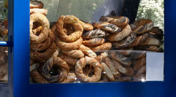 Stos świeżych obwarzanków w niebieskiej budce. Widać obwarzanki z makiem, sezamem i posypką serową.