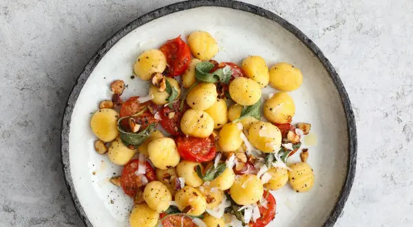 Pyszne makaron gnocchi z pomidorkami, szałwią i orzechami na talerzu.