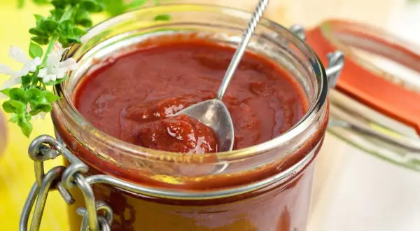 Domowy sos barbecue przepis. Słoik pełen pysznego, gęstego sosu, z łyżeczką do degustacji.