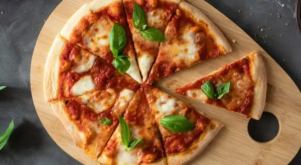 Ania gotuje ciasto na pizzę. Na drewnianej desce leży pyszna pizza margherita z bazylią, pokrojona na kawałki.