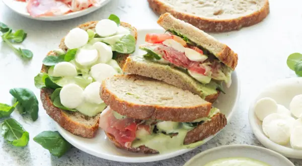 Pyszne włoskie kanapki z mozzarellą, szynką parmeńską i zielonym sosem na chrupiącym pieczywie.